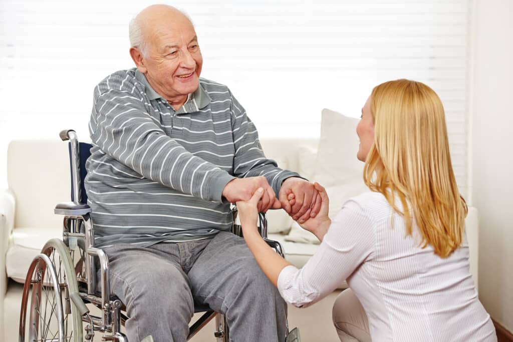 Woman holding hands of old man in wheelchair in a nursing home Woman holding hands of old man in wheelchair in a nursing home